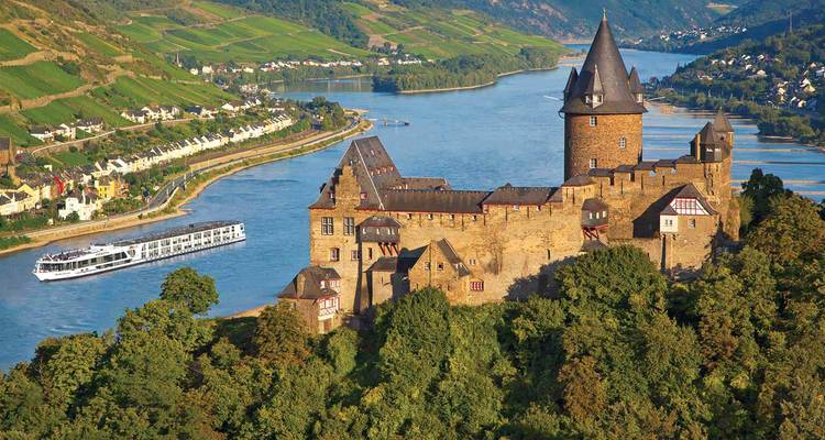 Majestic hilltop castle overlooking the Rhine River with a cruising ship passing below.