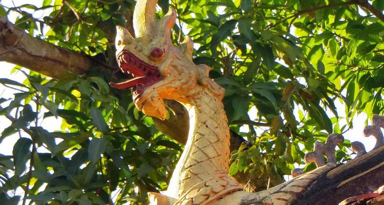Verwitterte Drachenskulptur auf belaubten Ästen in Laos
