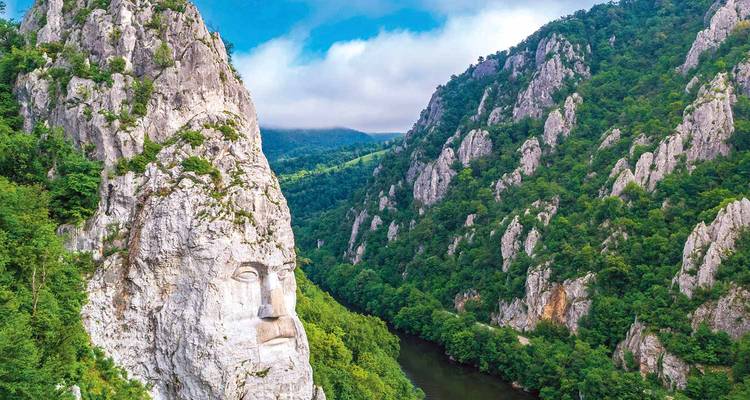 Giant rock-carved face of Decebalus overlooking the Danube gorge amid steep green cliffs