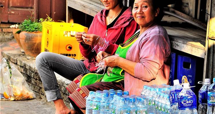 Zwei Frauen sitzen an einem Marktstand, an dem abgefülltes Wasser und handgefertigte Handwerksgüter verkauft werden.