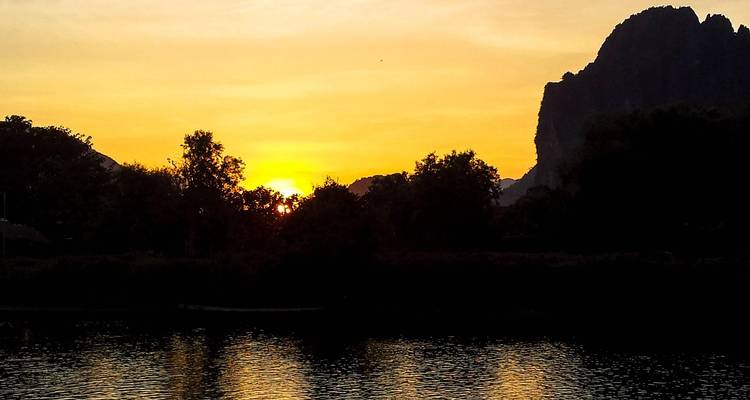 Ein feuerroter Sonnenuntergang senkt sich hinter silhouettierten Kalksteingipfeln, die sich in einem ruhigen Fluss spiegeln.