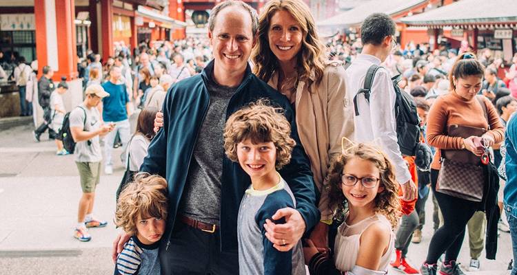 Smiling family of five amidst a bustling temple courtyard crowd.