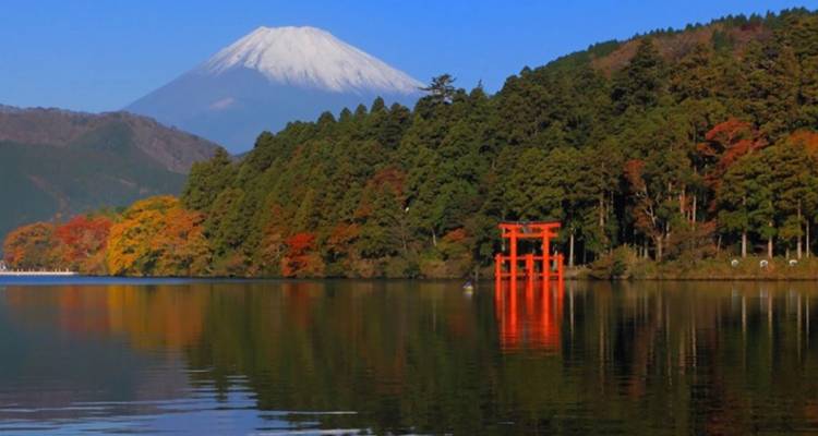 Calm lake reflecting autumn trees, red torii gate, and Mount Fuji under a clear blue sky