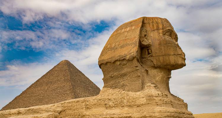 Statue emblématique du Sphinx avec la Pyramide de Khafre s'élevant derrière elle sous un ciel partiellement nuageux.