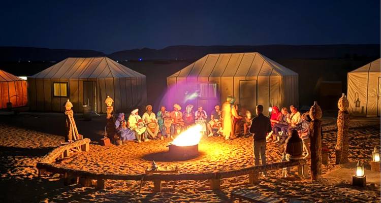 Camp désertique nocturne avec un groupe de personnes autour d'un feu ardent et des tentes en toile