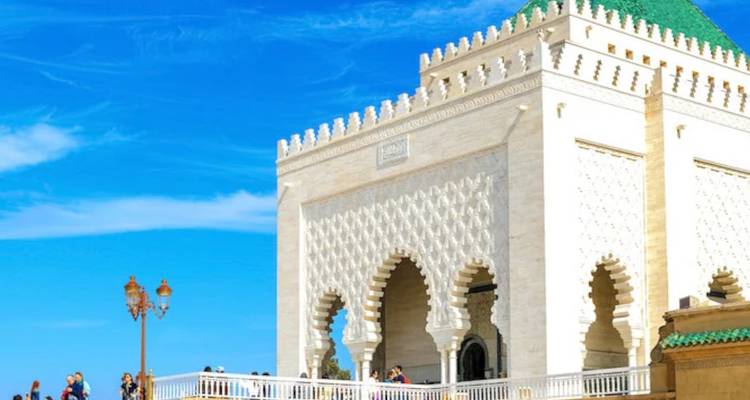 Les visiteurs se rassemblent près du mausolée en marbre blanc au toit recouvert de tuiles vertes à Rabat sous un ciel bleu.