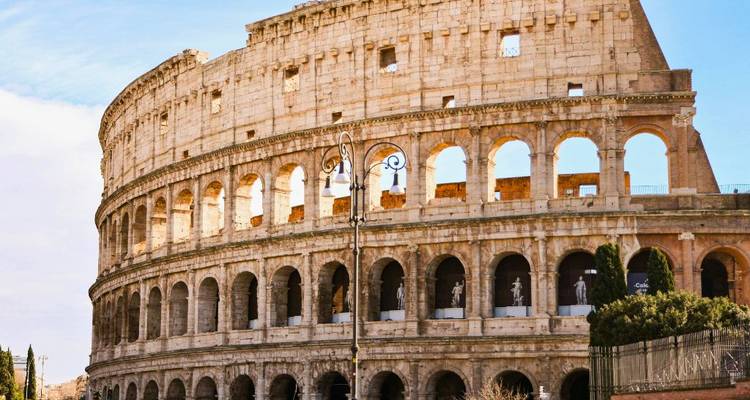 Closeup van de boog-vormige buitenmuren van het Colosseum in zonlicht tegen een blauwe hemel.