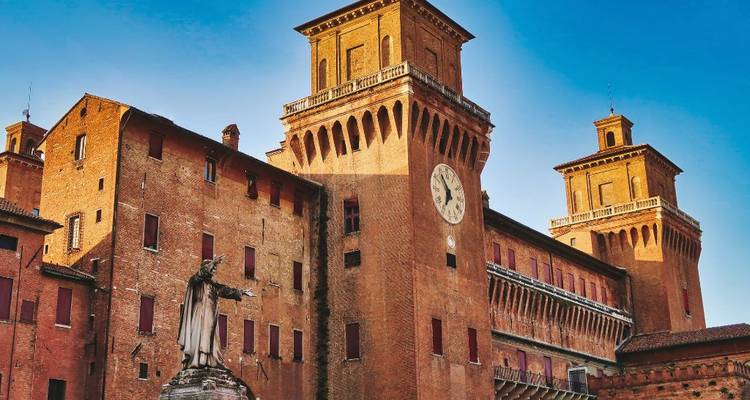 Rood bakstenen Este Kasteel in Ferrara met een centraal klokkentoren tegen een levendige blauwe achtergrond.