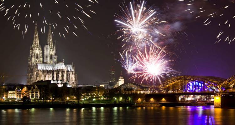 Nighttime fireworks explode above Cologne Cathedral and the illuminated Hohenzollern Bridge