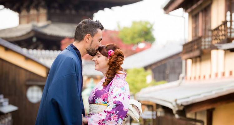 A man in traditional yukata kisses his partner’s forehead on a quiet Kyoto street near a historic pagoda.