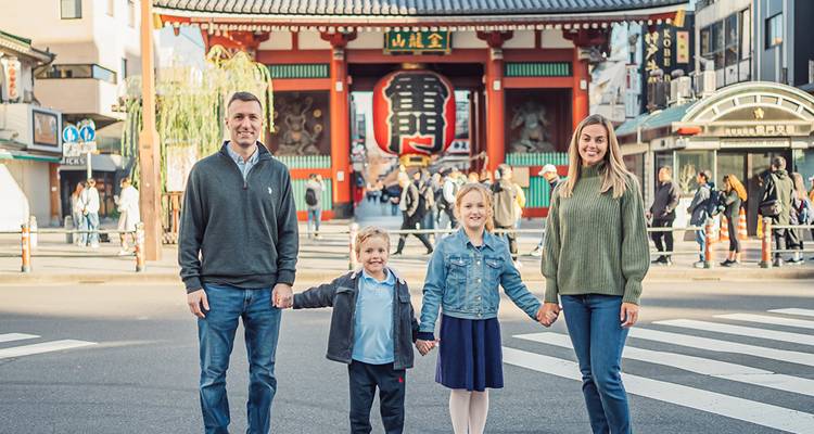 Family of four holding hands on a pedestrian crossing in front of Tokyo’s iconic Kaminarimon gate.