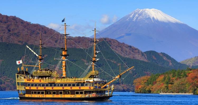 Historical-style sightseeing ship cruising on a deep blue lake with forested hills and Mount Fuji rising majestically in the distance.