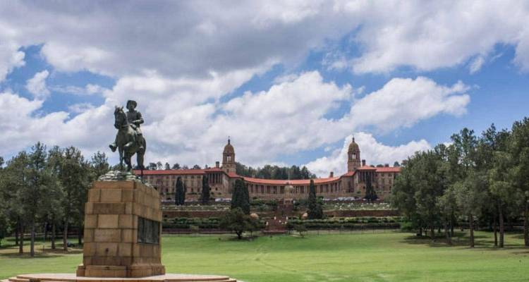 Pelouse panoramique menant aux Union Buildings avec une statue équestre au premier plan sous un ciel partiellement nuageux