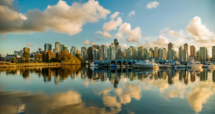 Downtown Vancouver’s skyline and marina are reflected perfectly in still water under a bright blue sky with scattered clouds.