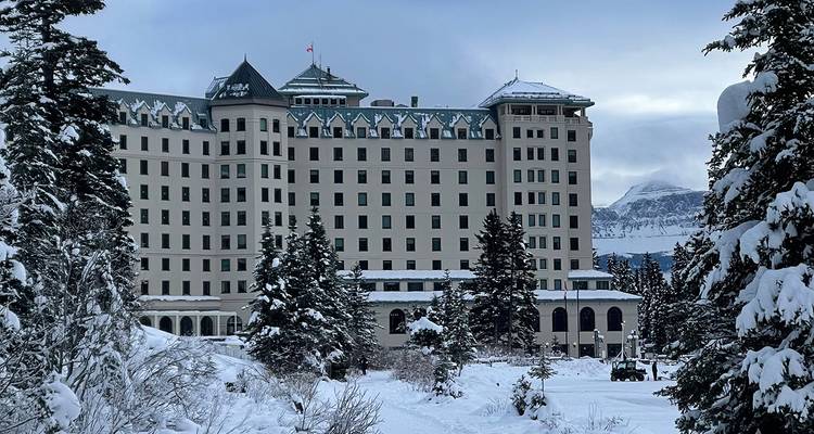 Historic grand hotel façade surrounded by snow-laden evergreens in a mountainous winter landscape.