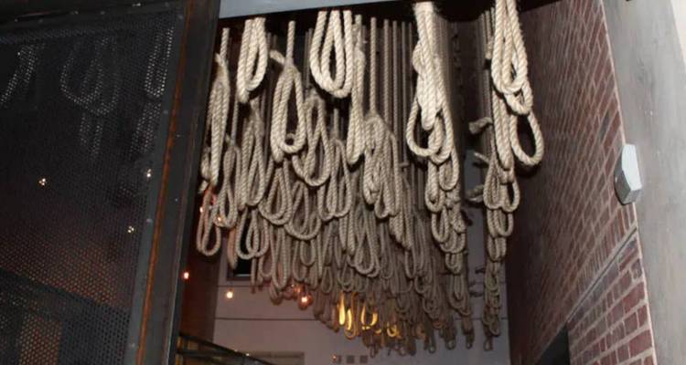 Installation artistique de nombreux nœuds coulants en corde suspendus dans un corridor de musée faiblement éclairé