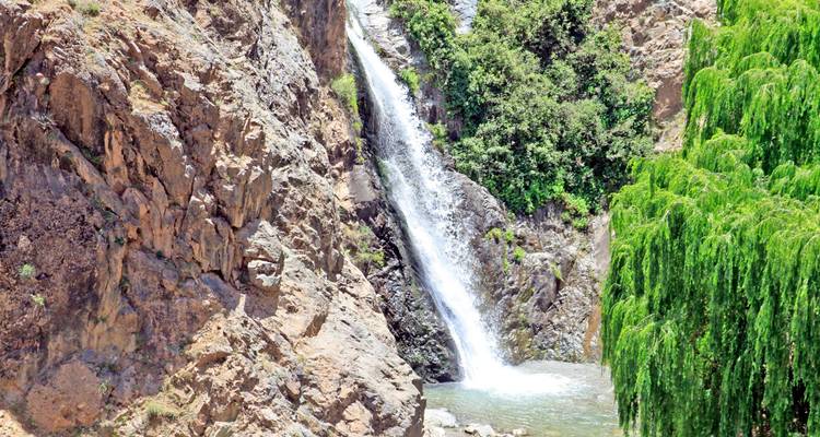 Une cascade étroite se précipite le long d'une falaise rocheuse entourée d'une végétation vert vif dans les montagnes de l'Atlas.