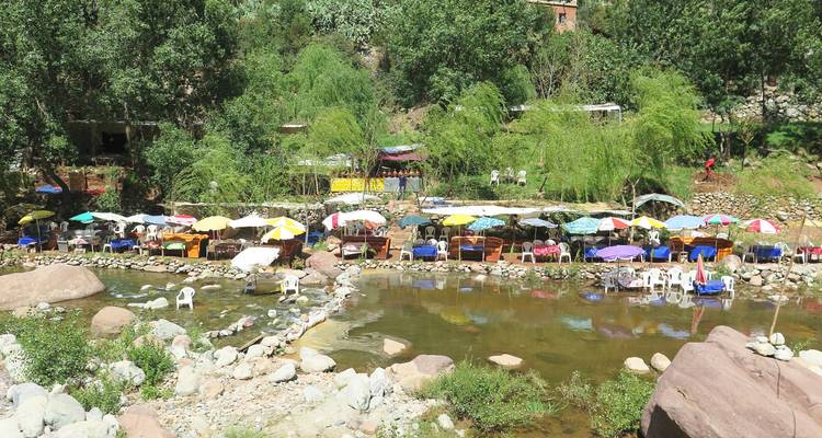 Des cafés riverains colorés avec des parasols et des chaises en plastique installés le long d'un cours d'eau peu profond dans les contreforts de l'Atlas.