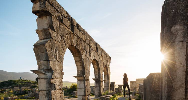 Le voyageur en silhouette explore les arches romaines éclairées par le soleil au milieu des ruines antiques de Volubilis.