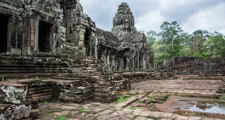 Weathered stone towers and terraces of a Khmer temple complex surrounded by jungle trees.