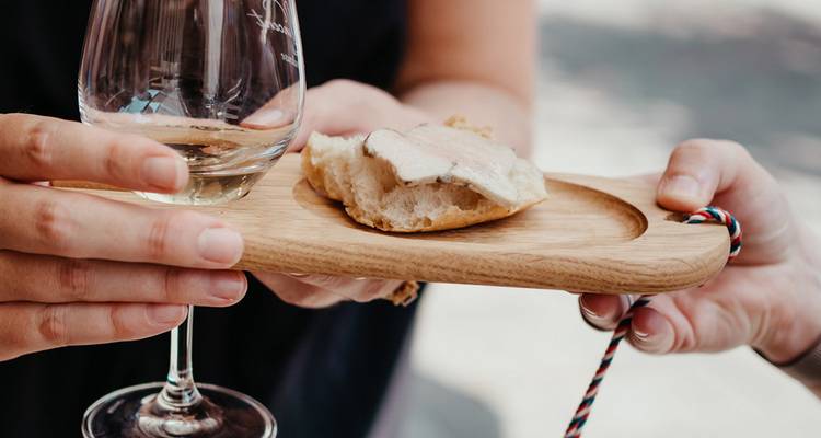 Hands holding a wine glass and a small plate of foie gras on bread during a tasting