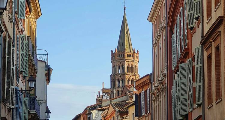 Narrow street flanked by pastel shutters and crowned by Toulouse's distinctive brick church spire