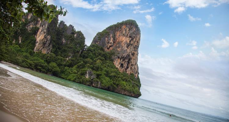 Tropical sandy beach meeting turquoise water and towering limestone cliffs beneath blue skies.