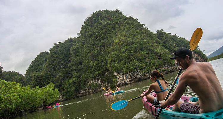 Kayakers paddle through mangroves and limestone karsts on a calm river.