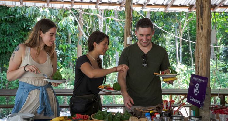 Travellers serve themselves tropical fruits and snacks at an open-air jungle shelter.