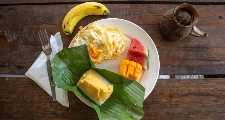 Thai breakfast plate with egg, mango, watermelon and sticky rice wrapped in banana leaf.