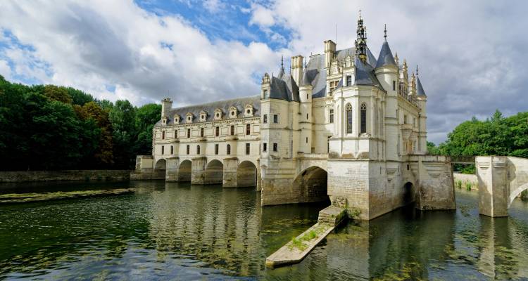 Château de Chenonceau spanning the River Cher under a partly cloudy sky.