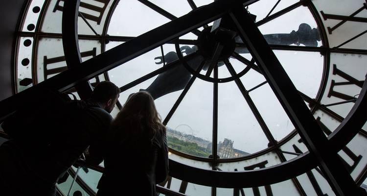 Silhouetted couple looking through the giant clock window of Musée d'Orsay toward the Paris skyline.