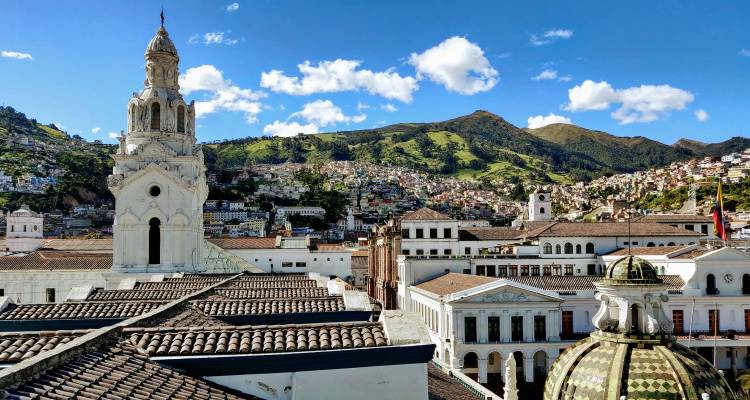 Panoramic view over colonial Quito rooftops with surrounding green Andes mountains.