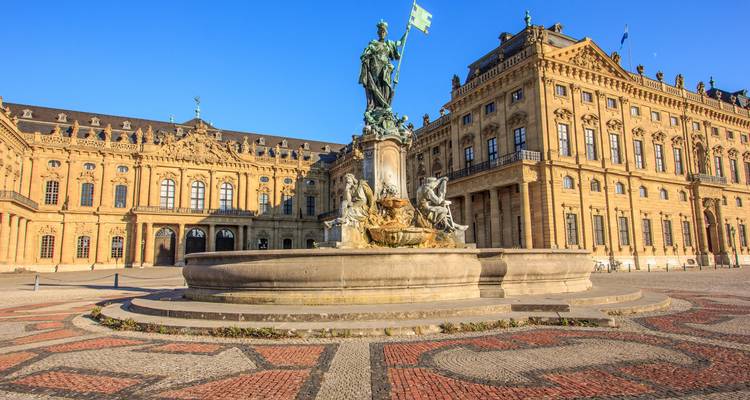 Baroque Würzburg Residence with ornate fountain and patterned square lit by afternoon sun.