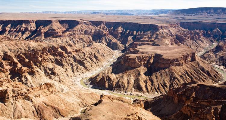 Vista expansiva hacia las profundidades dramáticas y erosionadas del Cañón del Río Fish con un río sinuoso abajo.