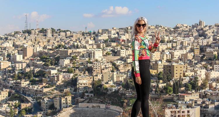 Woman stands on hill overlooking the sprawling beige cityscape of Amman.