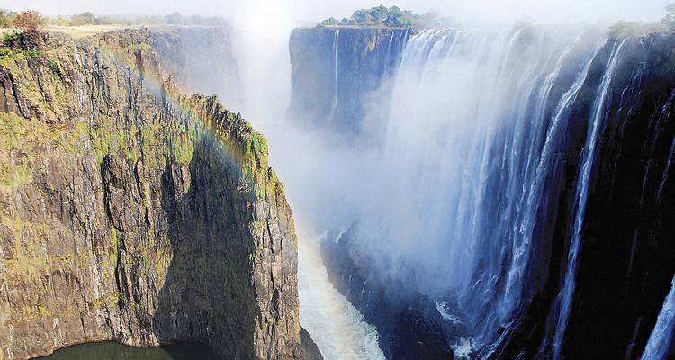 Poderosos velos de agua se desploman en una garganta profunda en las Cataratas Victoria con un arco iris vivido.