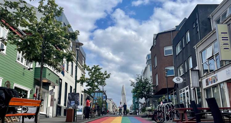 Rue aux couleurs de l'arc-en-ciel vibrant menant à la Hallgrímskirkja avec des piétons et des cafés.