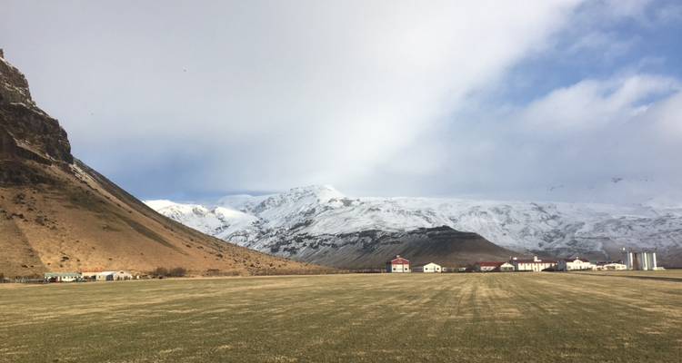 Vallée herbacée et vaste encadrée par des pics enneigés et un ciel partiellement nuageux.