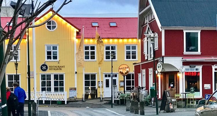 Rue accueillante de Reykjavik avec des maisons en bois aux couleurs vives éclairées par des ampoules chaleureuses.