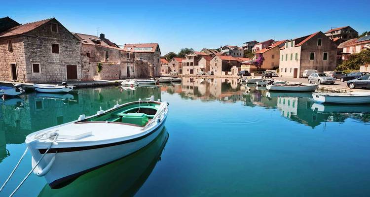 Village de pierre avec port de calme eau turquoise et petits bateaux amarrés par une journée dégagée