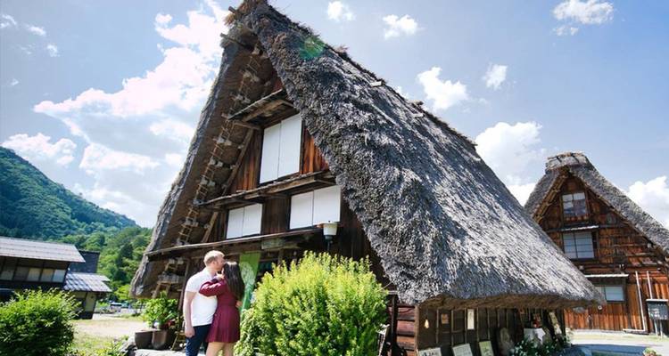 Paar, das sich vor einem traditionellen Strohdachhaus im Gassho-Zukuri-Stil in Shirakawa-go umarmt.