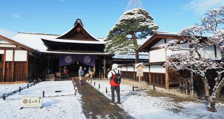 Schneebedecktes traditionelles Holzgebäude in Takayama mit Besuchern, die den Innenhof erkunden.
