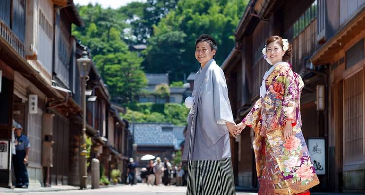 Lachendes Paar in traditioneller Kimono haelt Haende auf einer historischen Holzstrasse, die von Teehaeusern gesaeumt wird.