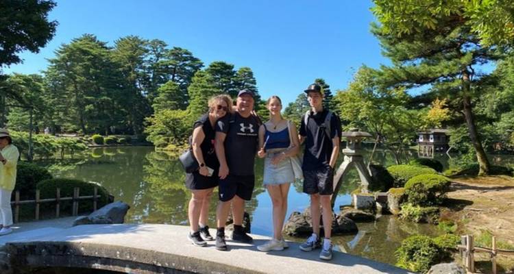Vier Reisende posieren gemeinsam auf einer Steinbrücke über einem ruhigen Teich in einem üppigen japanischen Garten.