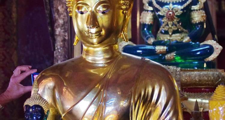 Glanzend gouden Boeddhabeeld in zwak verlichte tempel met hand van een aanbidder die een camera vasthoudt
