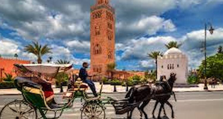 Calèche tirée par des chevaux passant devant le minaret de la Koutoubia sous des nuages dramatiques à Marrakech.