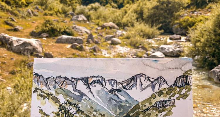 Un esbozo en acuarela portátil de las crestas de montaña está alineado con el paisaje real detrás de él.