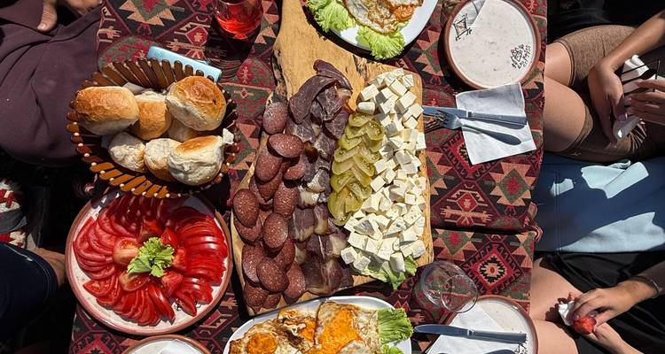 Tradicional picnic albanés con tomates frescos, quesos, carnes y pan sobre una alfombra estampada en el exterior.
