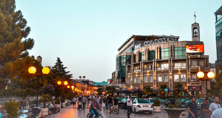 El bullicio de la tarde en una avenida peatonal en el centro de Tirana con el edificio Colosseo iluminado.